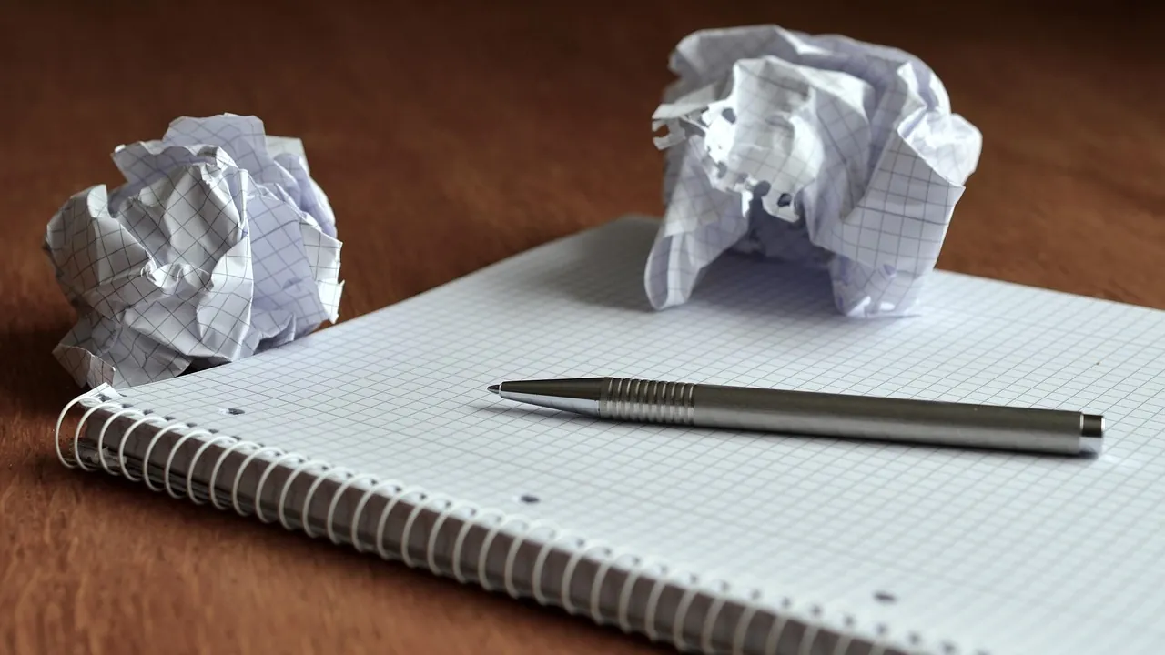 Un bloc quadrillé, un stylo, et deux feuilles froissées mises de côté